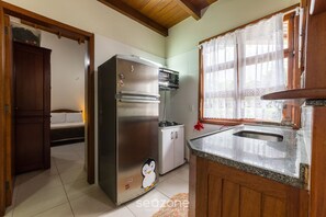 A compact kitchen with a refrigerator, oven, and microwave. There's a bed in the adjacent room and a window with lace curtains. - 2-bedr Ap W/bbq, 400m From the Beach Jurere Jba202 (Florianópolis)