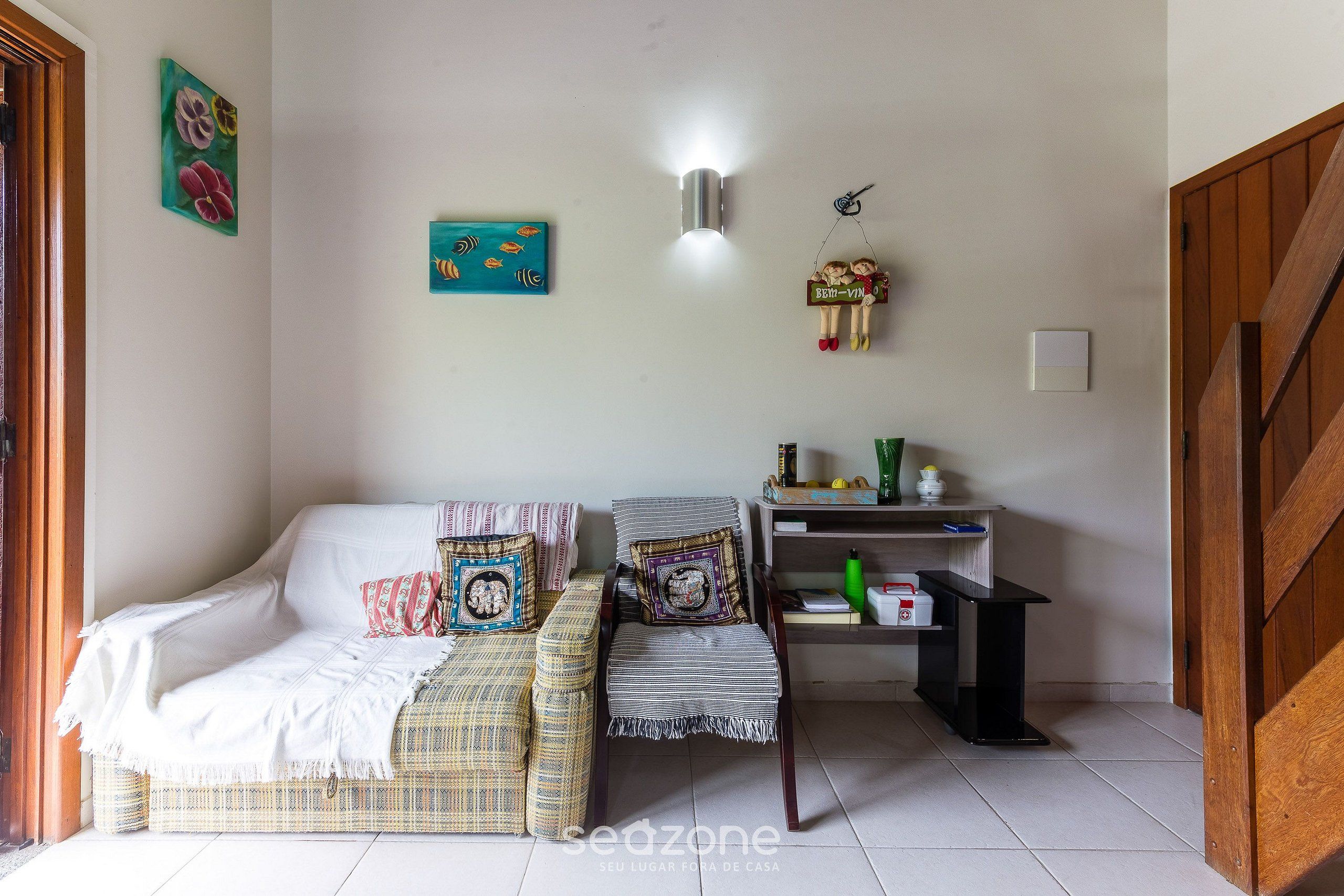 A cozy living room with a sofa, a chair, and a small table. There are wall decorations and a light fixture.