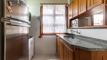 Una cocina compacta con armarios de madera, un refrigerador de acero inoxidable y una ventana con cortinas de encaje.