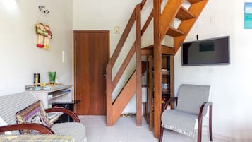 Una sala de estar con una escalera de madera, un televisor montado en la pared y dos sillones.