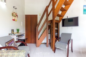 A living room with a wooden staircase, a television mounted on the wall, and two chairs. - 2-bedr Ap W/bbq, 400m From the Beach Jurere Jba202 (Florianópolis)