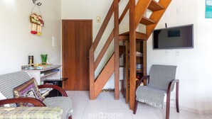 A living room with a wooden staircase, a television mounted on the wall, and two chairs. - 2-bedr Ap W/bbq, 400m From the Beach Jurere Jba202 (Florianópolis)