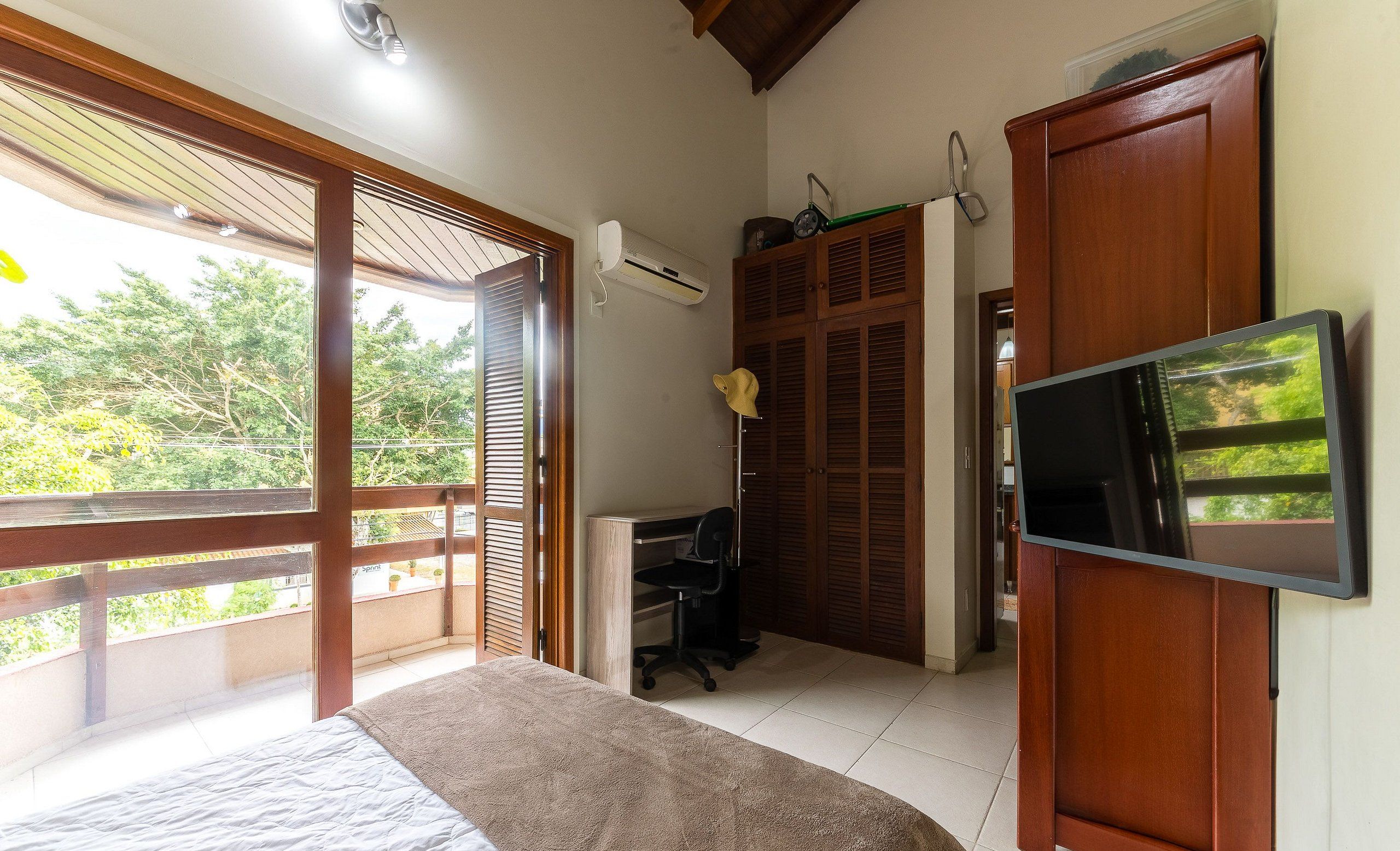 A bedroom with a bed, a desk, a chair, an air conditioner, and a TV.