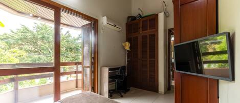 A bedroom with a bed, a desk, a chair, an air conditioner, and a TV.