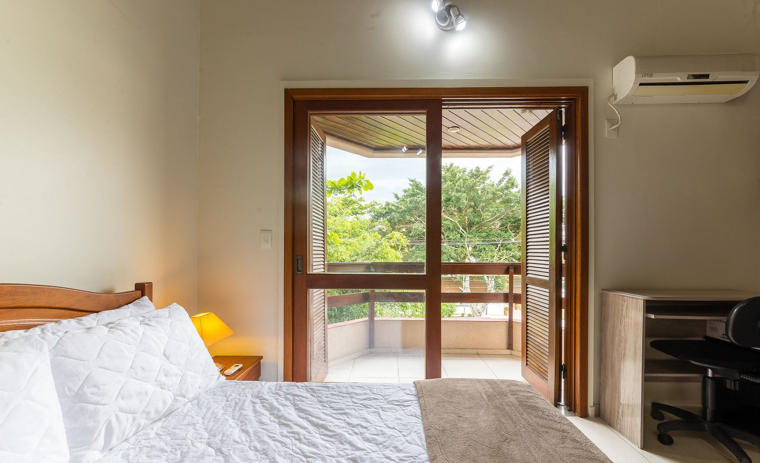 Un dormitorio con cama, escritorio y vista a un balcón.