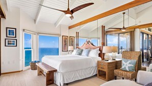 A spacious bedroom with a large bed, a ceiling fan, a view of the ocean, and a balcony.