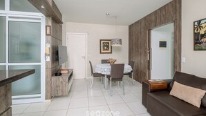 Una sala de estar moderna con un sofá marrón, una mesa de comedor con sillas y una cocina con refrigerador y televisor.