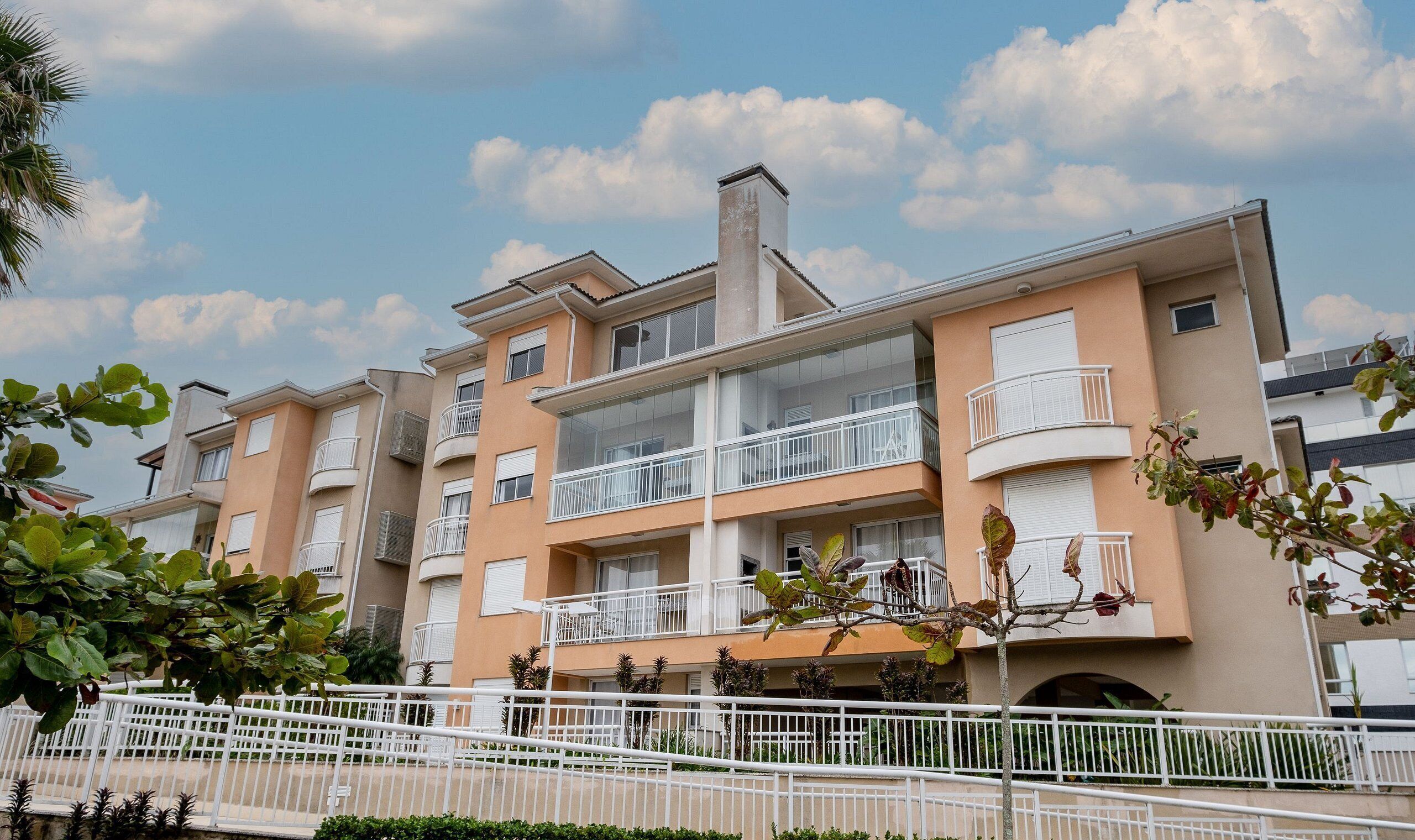 A multi-story residential building with balconies, a white fence, and a clear sky.