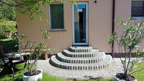 Un edificio con una puerta que indica '4 APARTMENT BUILDING', una escalera de piedra circular y plantas en macetas.