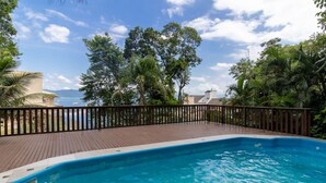 A swimming pool with a wooden deck, surrounded by lush greenery and a view of the sea. - Sea View Apt 240m From the Beach in Jurere Ido207 (Florianópolis)