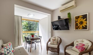 Un salon moderne comprenant un coin repas, un téléviseur fixé au mur et une grande fenêtre avec des rideaux.