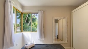 A bedroom with a bed, a window with curtains, a mirror, and a view of greenery outside. - Sea View Apt 240m From the Beach in Jurere Ido207 (Florianópolis)