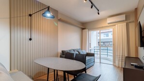 Una habitación de hotel moderna con una mesa de comedor, un sofá, un escritorio y un ventanal con cortinas.
