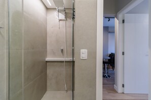 Un bagno moderno con cabina doccia in vetro, lavandino bianco e una presa di corrente a vista.