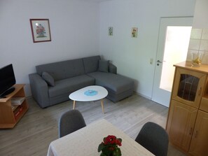 En stue med en grå sofa, et lille hvidt bord, et fjernsyn på et træstel og et skab.