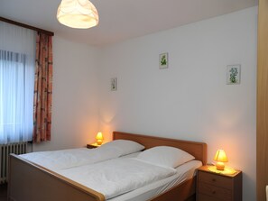En dobbeltseng med to sengeborde, hvert med en lampe, et vindue med gardiner og et billede på væggen.