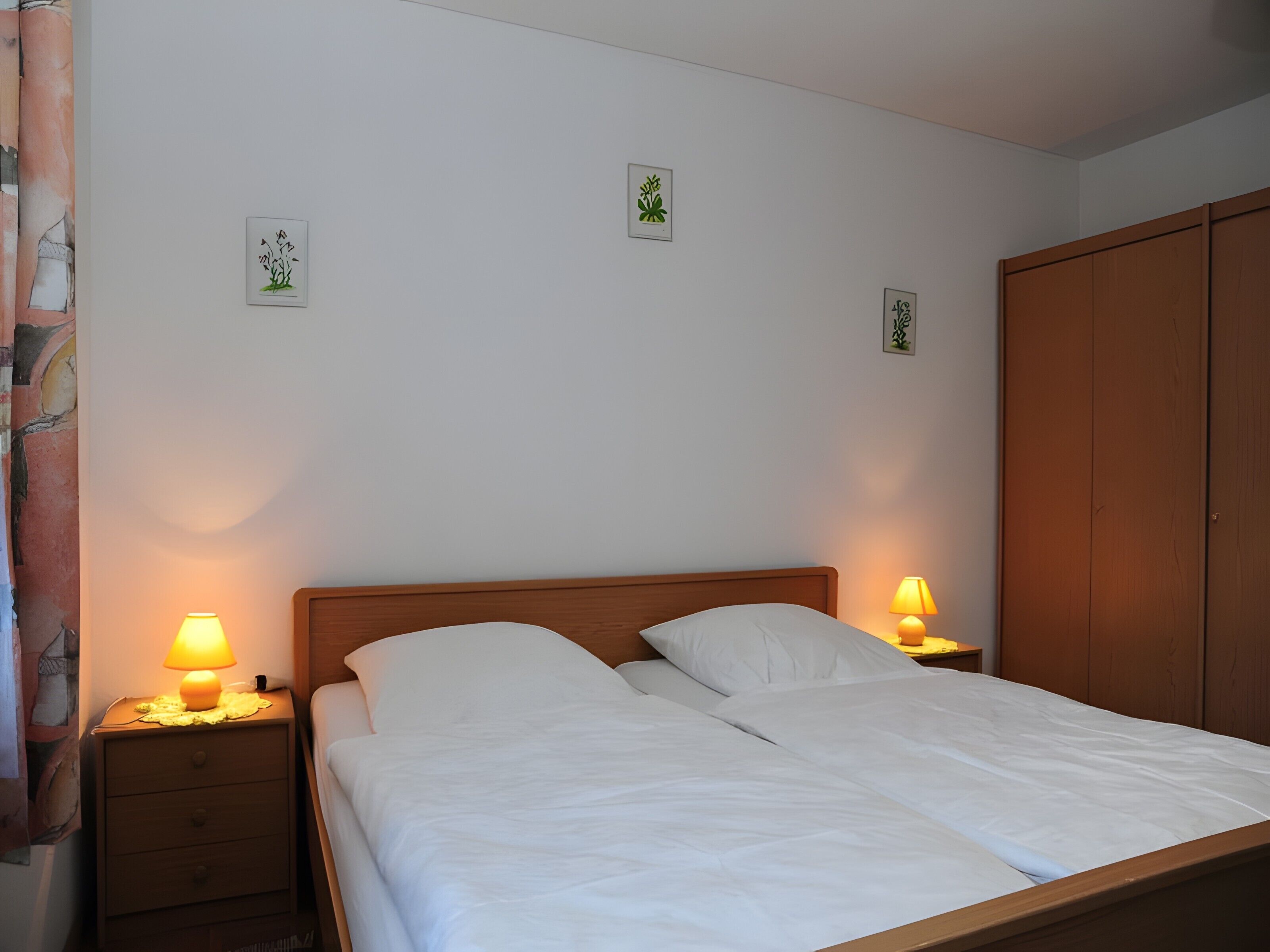 Un lit bien fait, avec deux oreillers, une tête de lit en bois, deux lampes de chevet, une table de chevet et une armoire.