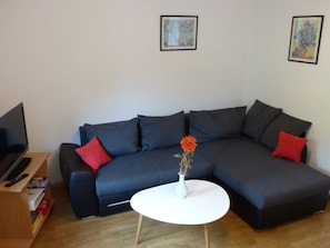 A modern living room with a dark grey sectional sofa, a white coffee table, and a vase with flowers. - Apartment 'Nr 2' with Shared Terrace, Shared Garden and Wi-Fi (Simonswald)