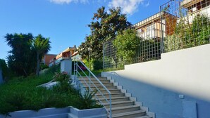 A concrete staircase leading up to a building with a metal fence and greenery around.