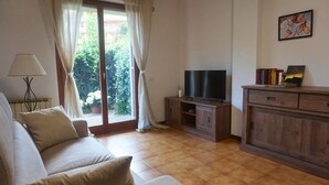 A living room with a sofa, a TV on a wooden cabinet, and a view through a large window.