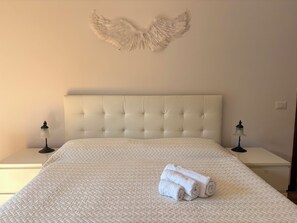 A bedroom with a tufted headboard, a quilted bedspread, two bedside tables with lamps, and a wall-mounted decorative piece. - Casa dell'angelo labaro (Roma)