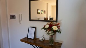 A reception desk with a framed menu, a vase of flowers, a small statue, and a mirror above.