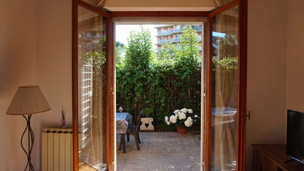 An open sliding glass door leading to an outdoor patio with a table, chairs, and a potted plant.