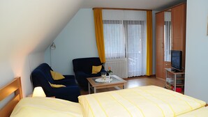 Ein Hotelzimmer mit Bett, Sessel, kleinem Tisch, Fernseher und einem Fenster mit Vorhängen.