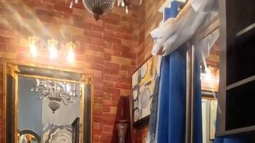 A bathroom with a brick wall, a chandelier, a mirror with a gold frame, and blue curtains.