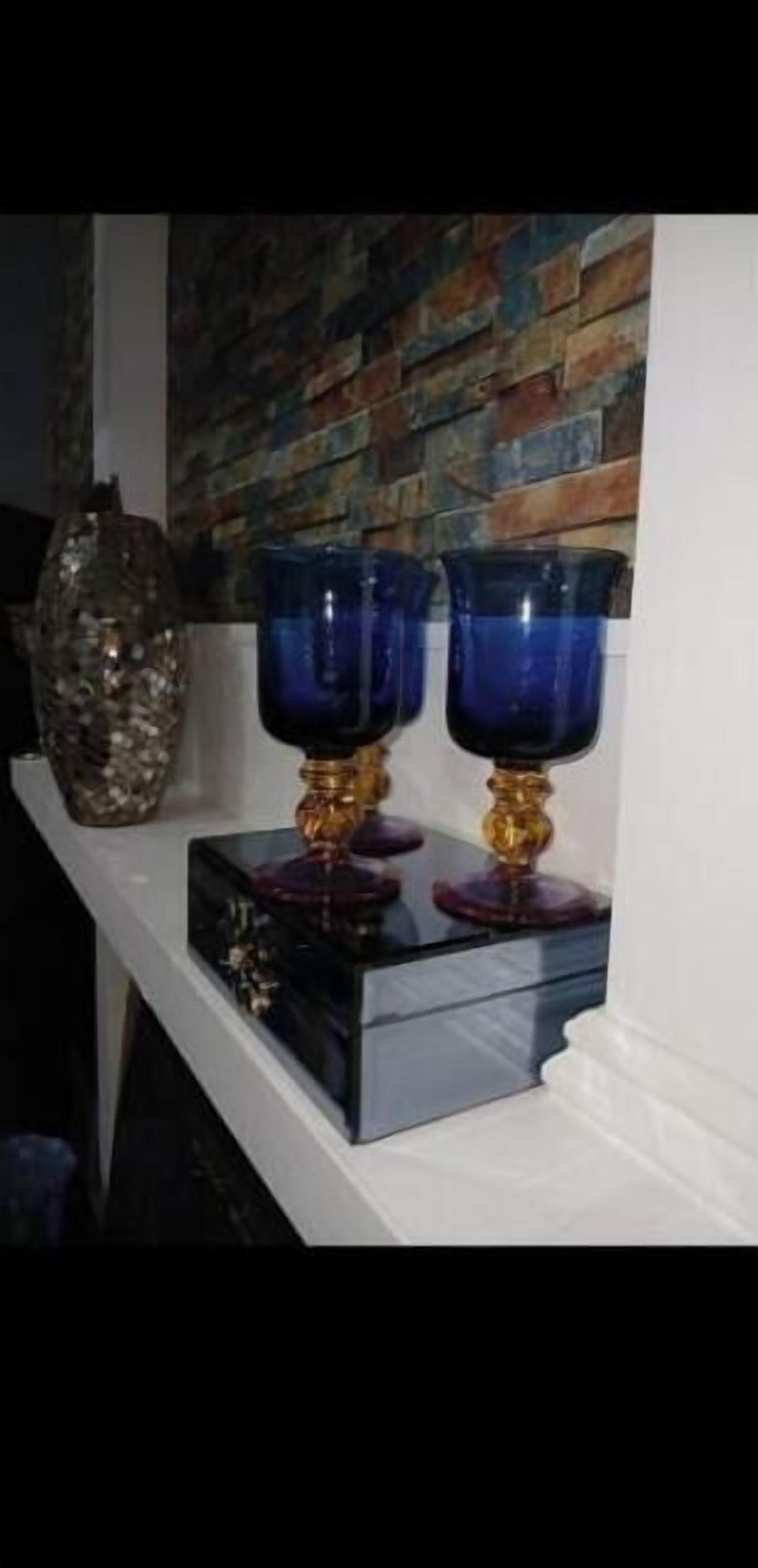 Une étagère sur laquelle reposent deux vases en verre bleu, le tout adossé à un mur blanc orné d’un motif en briques.