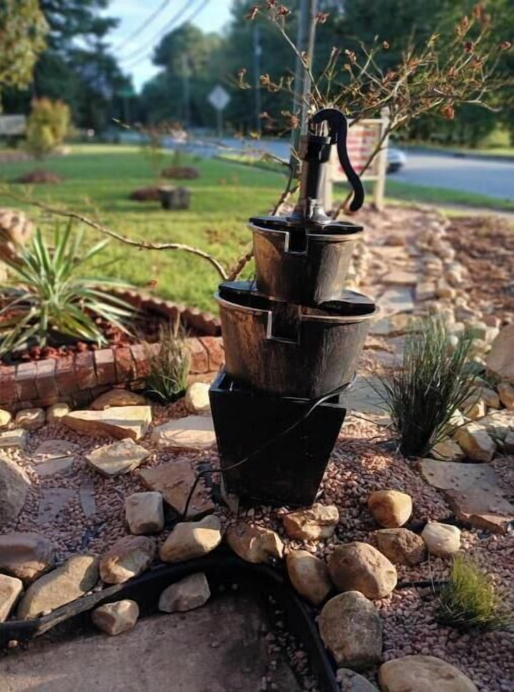 A garden with a tall, black, tiered planter structure surrounded by rocks and small plants.