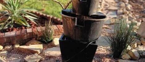 A garden with a tall, black, tiered planter structure surrounded by rocks and small plants.