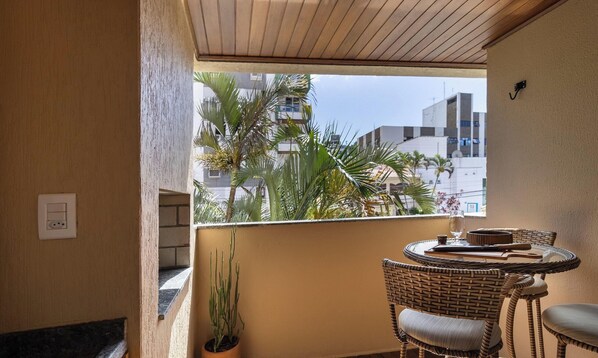Un balcon agrémenté de meubles en osier, d’une plante en pot et offrant une vue sur des immeubles et des palmiers.