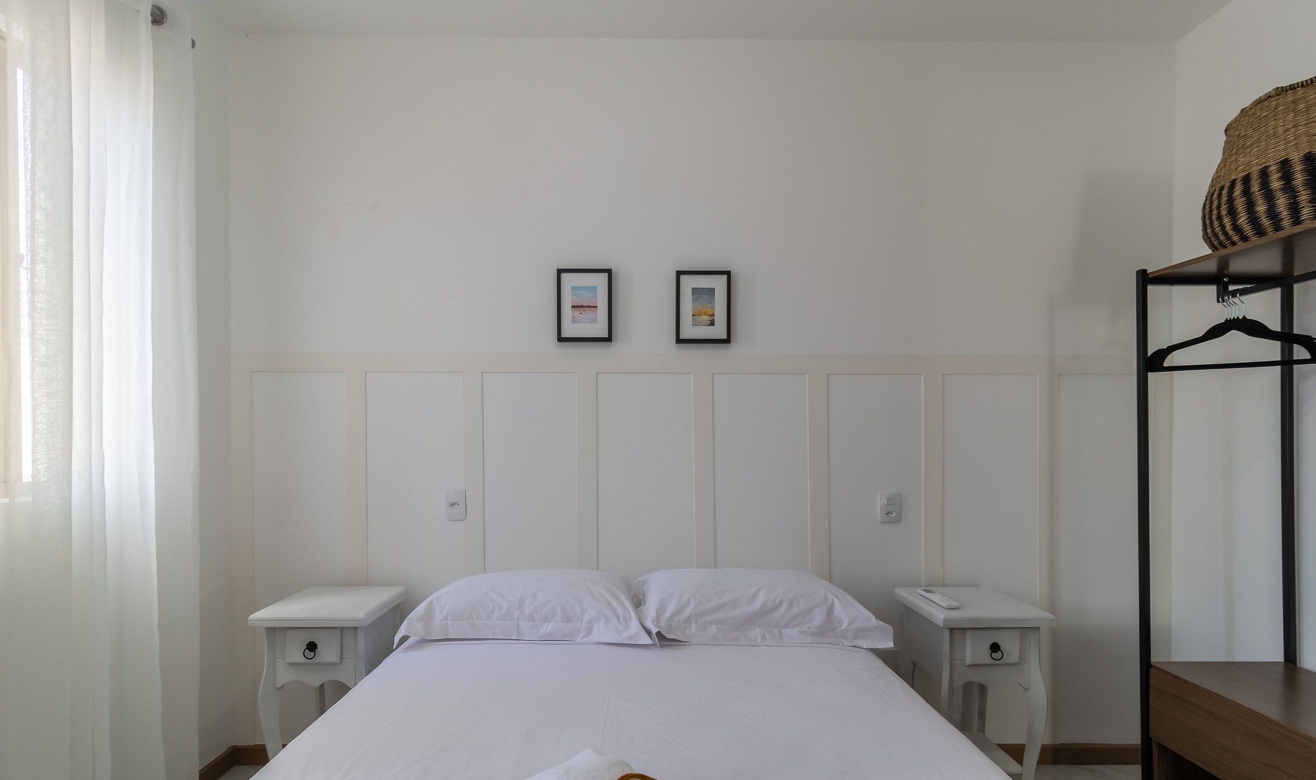 A bedroom with a bed, two bedside tables, a wardrobe, and two framed pictures on the wall.