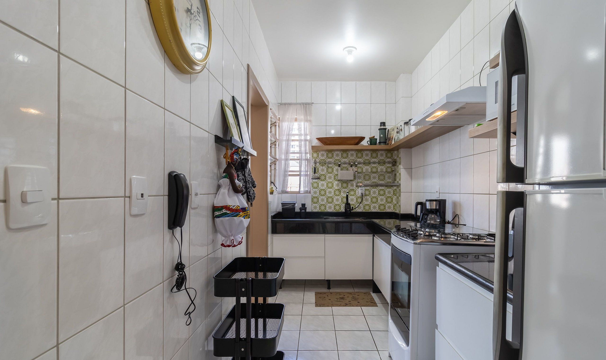 A modern kitchen with white cabinets, a gas stove, a refrigerator, and a window with curtains.