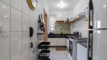 A modern kitchen with white cabinets, a gas stove, a refrigerator, and a window with curtains.