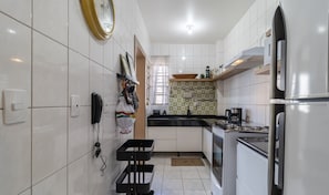 Une cuisine moderne avec des meubles blancs, une cuisinière à gaz, un réfrigérateur et une fenêtre avec des rideaux.