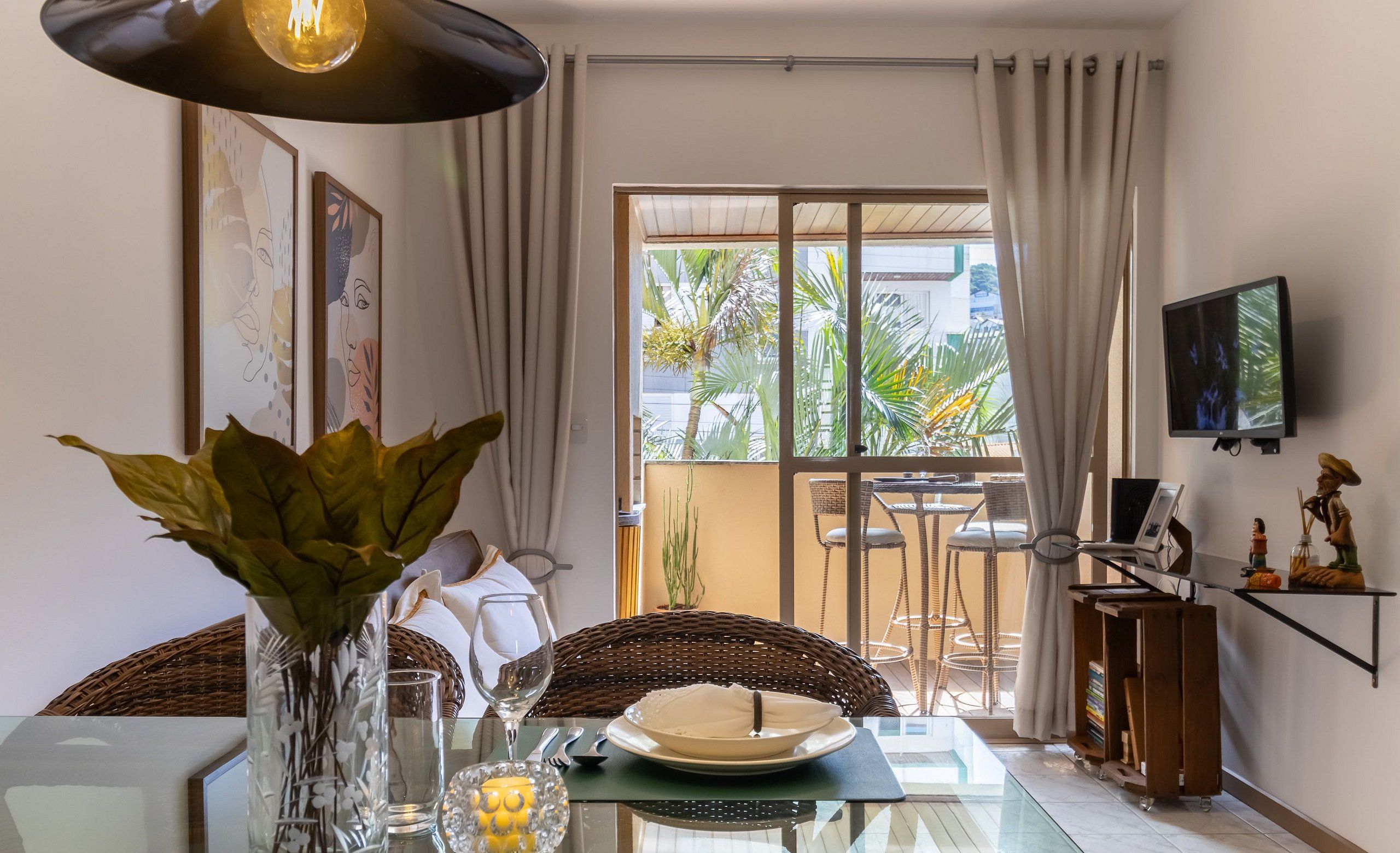 A dining area with a glass table, a vase with green plants, a candle, and a dining set.