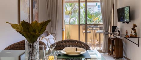 A dining area with a glass table, a vase with green plants, a candle, and a dining set.