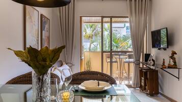 A dining area with a glass table, a vase with green plants, a candle, and a dining set.