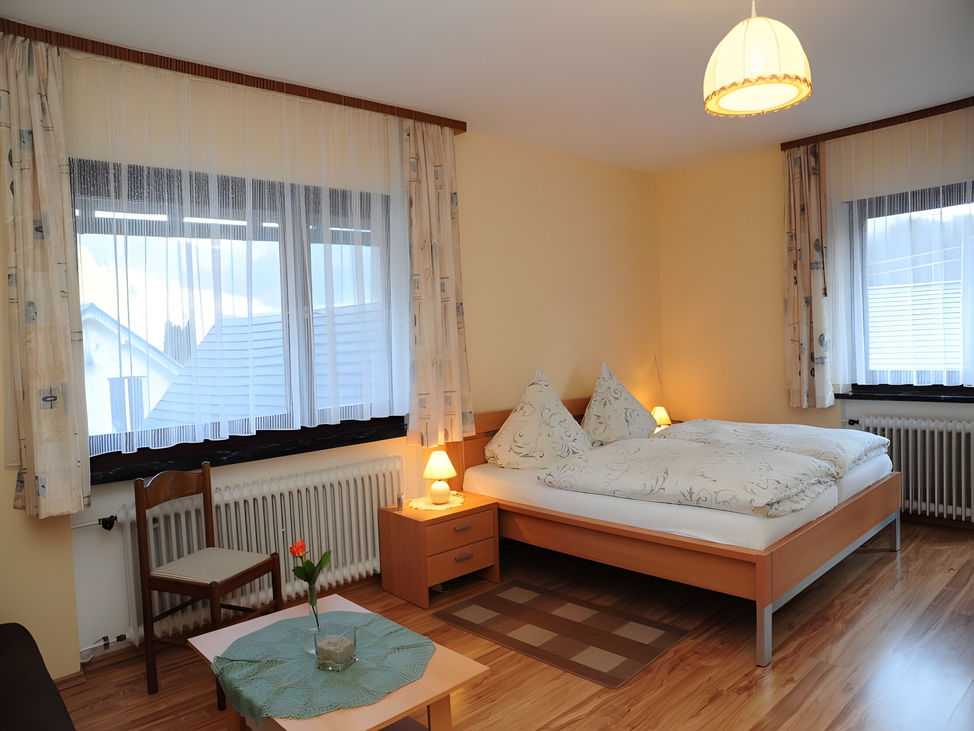 Ein Schlafzimmer mit Bett, Nachttisch, Lampe, Stuhl und Blick ins Freie.