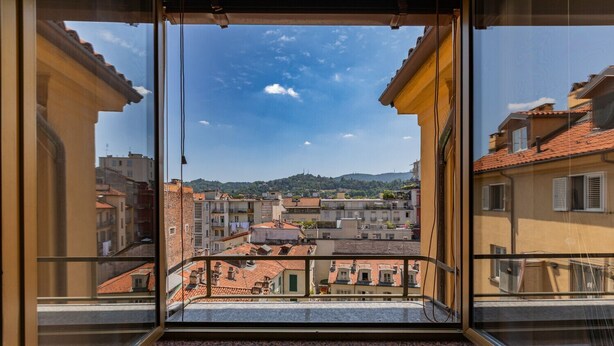 Un balcón con vista a un paisaje urbano, que presenta tejados de terracota y edificios con balcones.