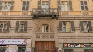 Un edificio con una entrada central, varias ventanas con contraventanas y un pequeño balcón con barandilla decorativa.