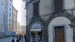 A street with a building featuring a wooden door and a shop with postcards. - Florence Dome Rooms (Florence)
