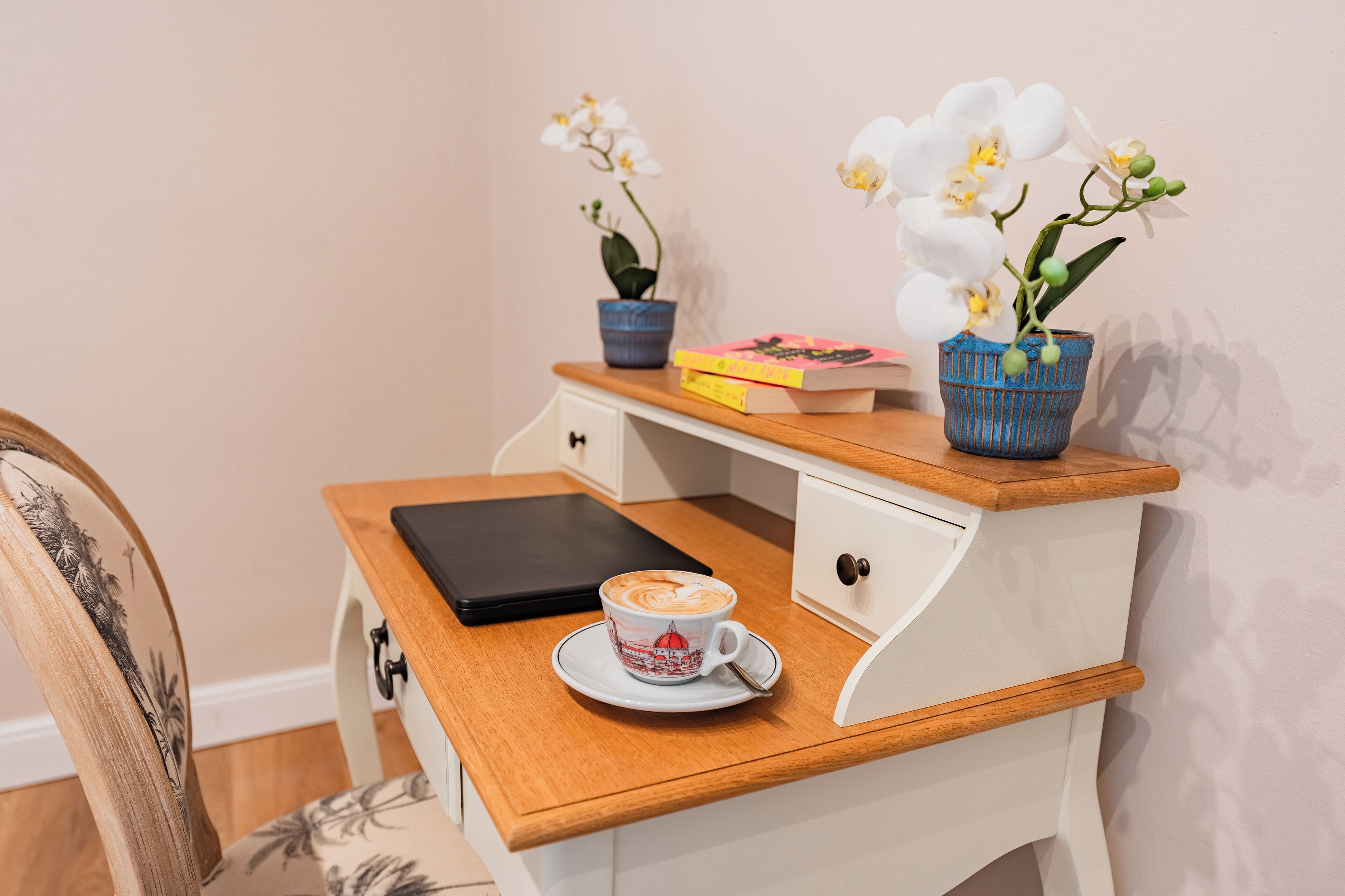 A wooden desk with a laptop, a cup of coffee, and two potted orchids.
