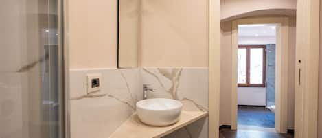 A bathroom with a marble sink, a mirror, and a shower.