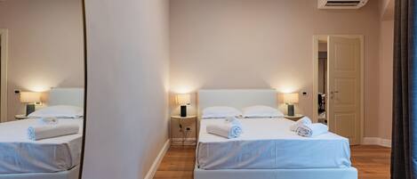 A hotel room with two beds, bedside tables with lamps, an air conditioning unit, and a door.
