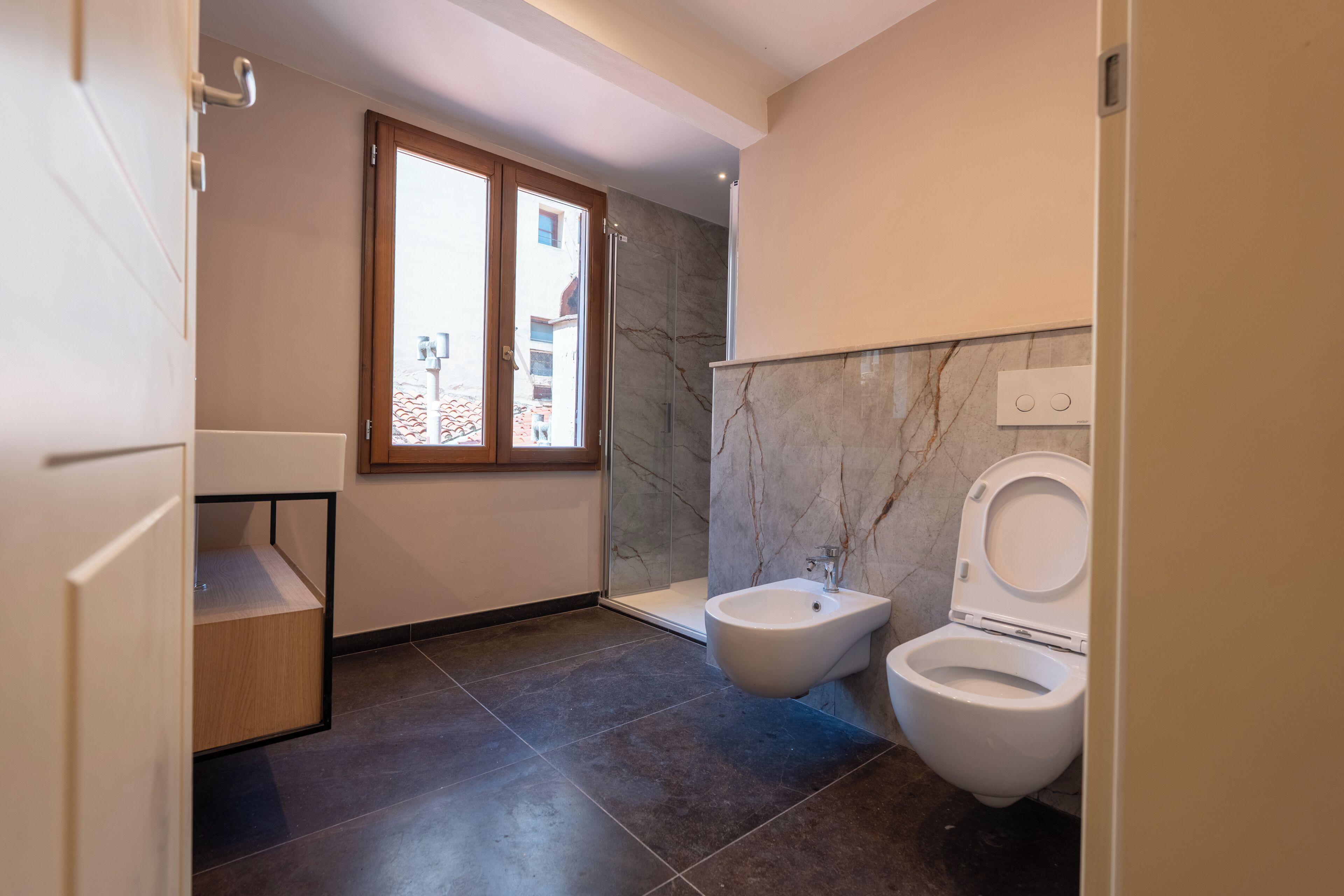 Un baño moderno con bidé, inodoro y ventana que proporciona luz natural.