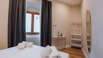 Ein Hotelzimmer mit Bett, Handtüchern, einem Heizkörper, einem kleinen Tisch mit einer Weinflasche und einer Pflanze, einem Spiegel und einem Kleiderschrank.