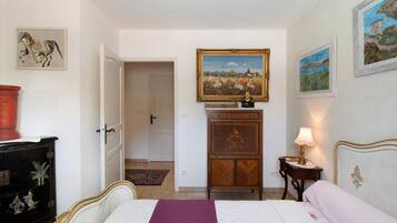 Een slaapkamer met een bed, nachtkastje, dressoir en een deur die naar een andere kamer leidt.